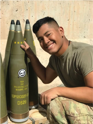 member of the US Army smiles next to a missile with an Alpha Coffee sticker on it